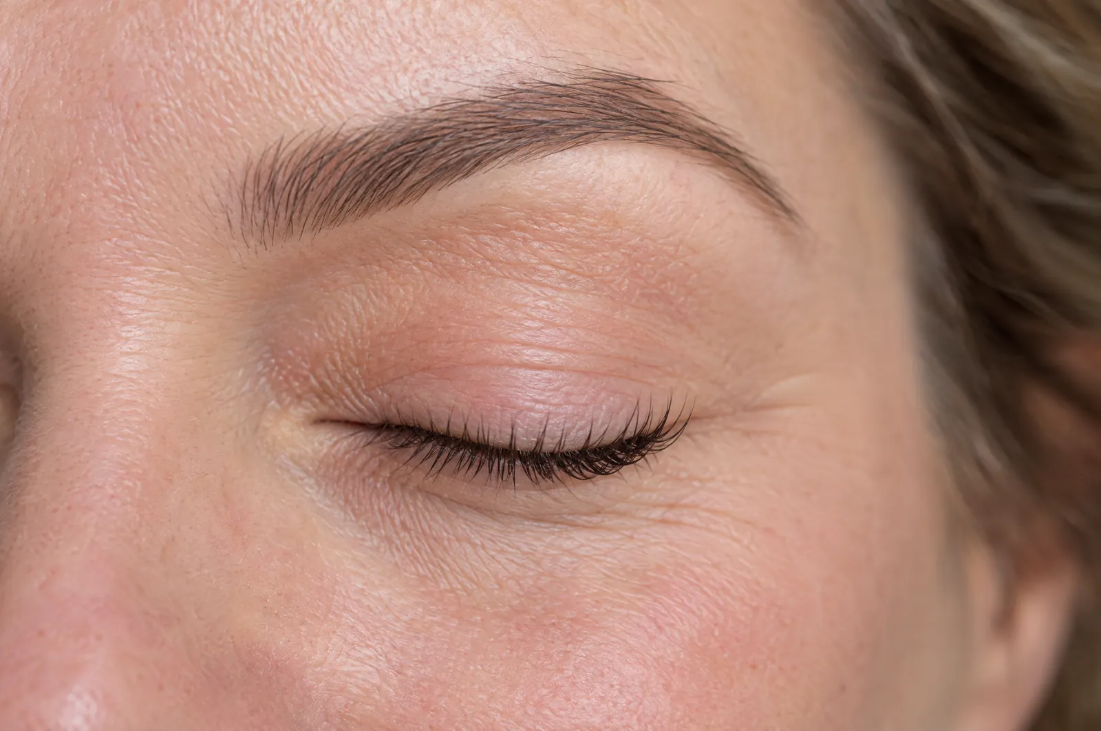 Geschlossenes Auge mit natürlich geschwungenen Wimpern und gepflegter Braue